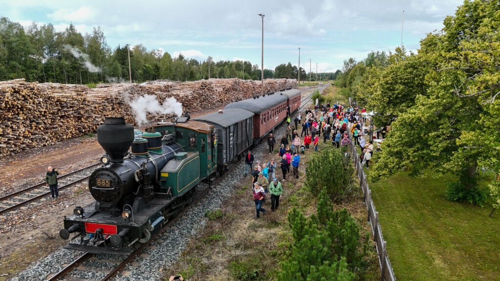 Joroisten rautatieasema ilmakuvassa idästä päin. Vasemmalla radan takana isot puutavarakasat, keskellä ratapihalla höyryjuna ja oikealla ratapihalla ja asemarakennuksen pihalla arviolta 200-300 hengen väkijoukko.